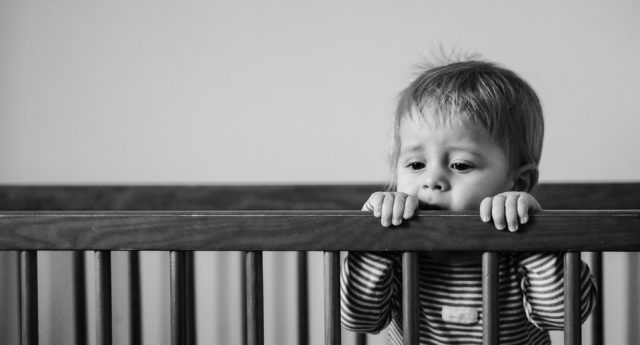 Ill toddler holding onto crib.