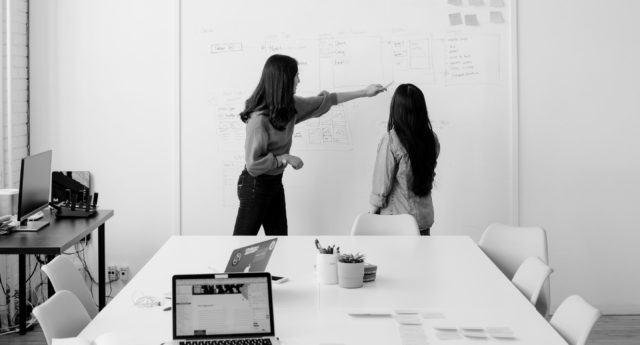 Women working at a whiteboard in a boardroom.